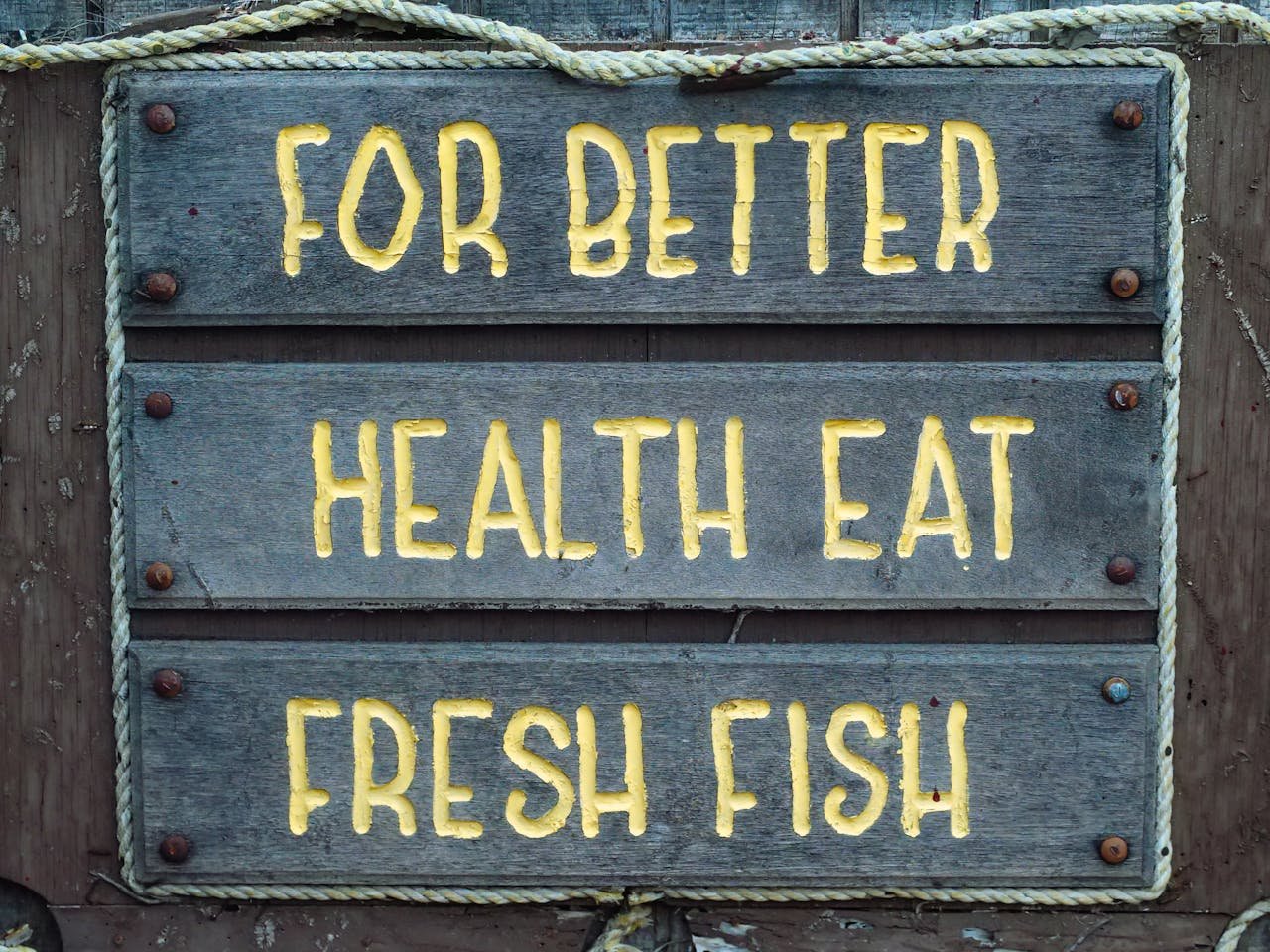 Wooden sign urging better health through fresh fish consumption, set against a rustic background.